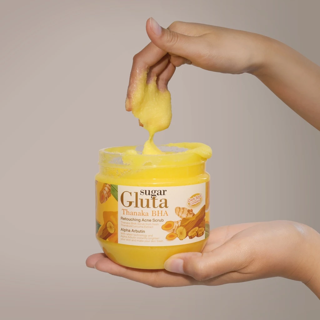 Hand holding a jar of 'Sugar Gluta' product with a yellow substance being scooped out.
