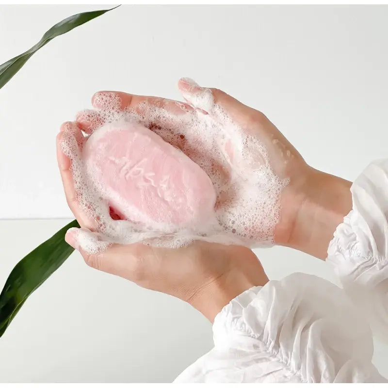 Pink bath bomb with bubbles held in hands against a light background